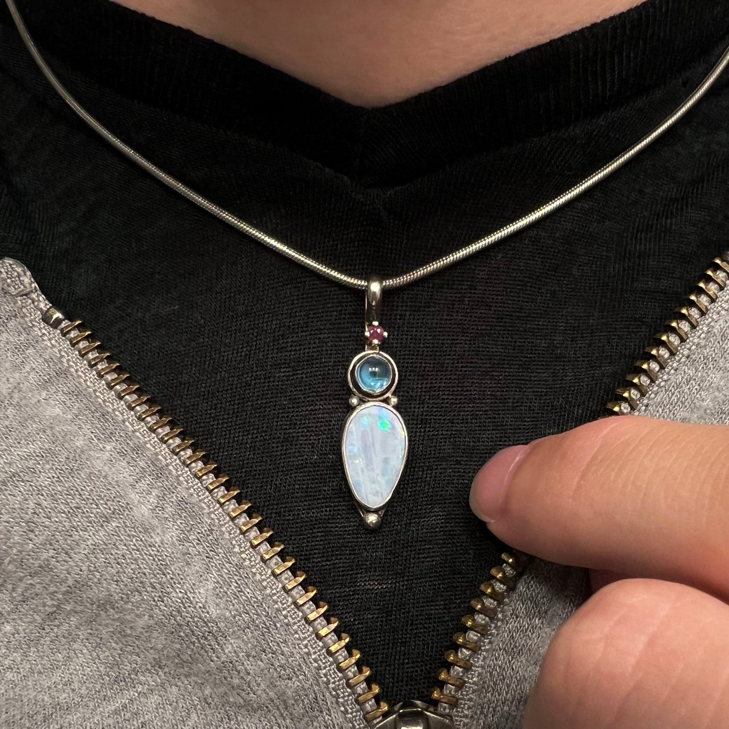 A sterling silver necklace shaped like a child, mounted with an opal doublet, a ruby, and a blue piece of glass.