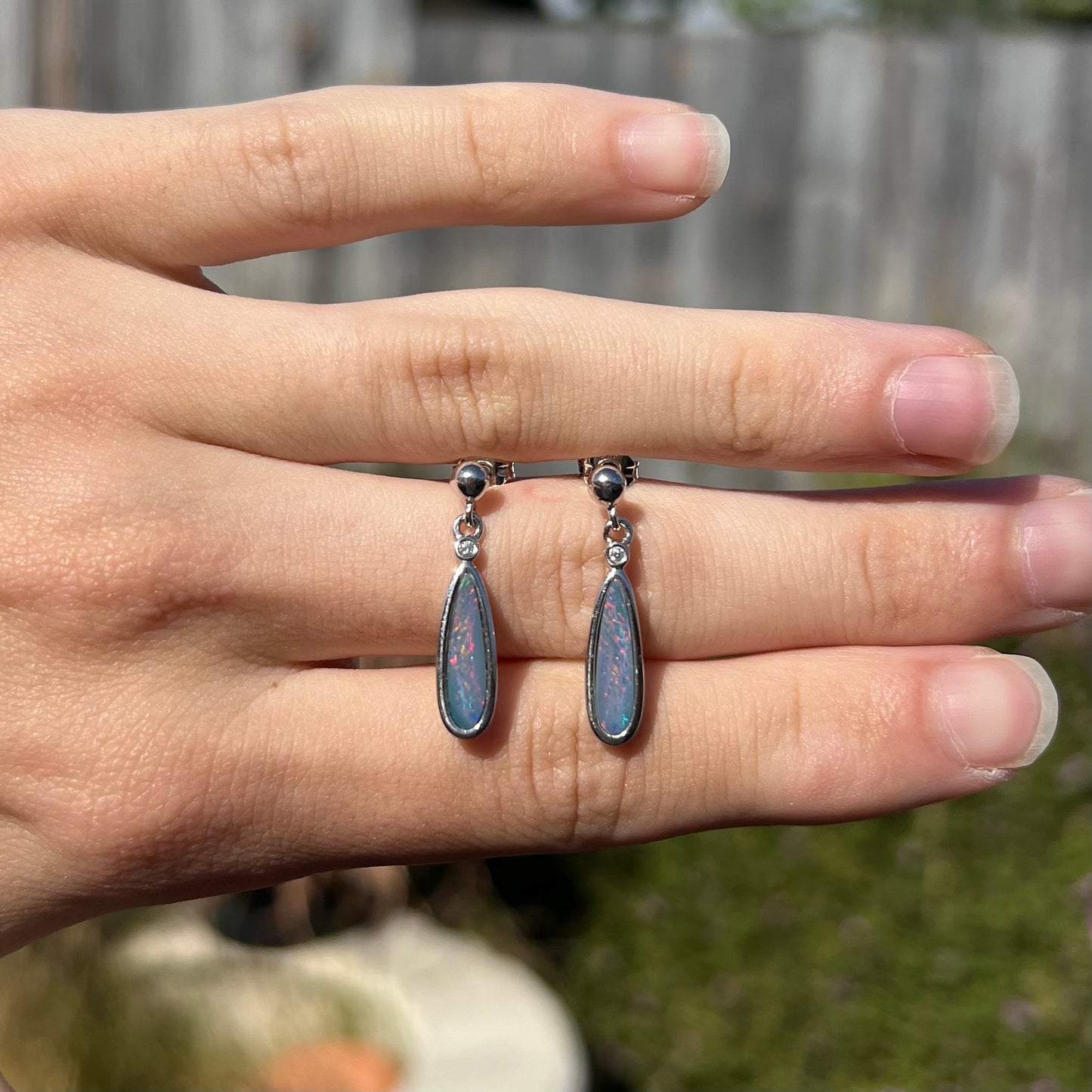 A pair of sterling silver, pear shaped opal doublet dangle earrings.  The opals have a gray body tone with red fire.