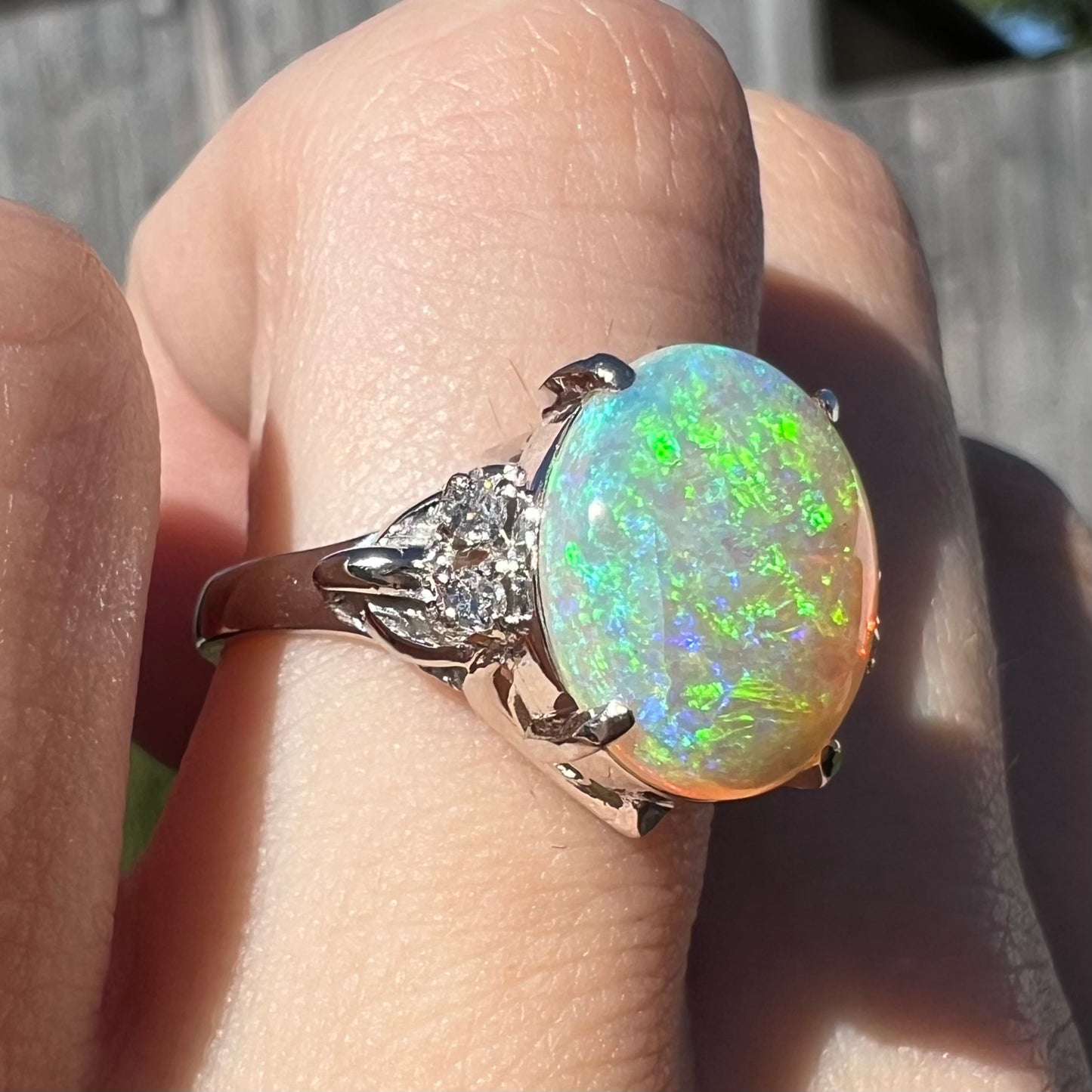 An Australian crystal opal engagement ring set with diamonds in a platinum filigree mounting.  The opal plays green/blue colors and has a crack.