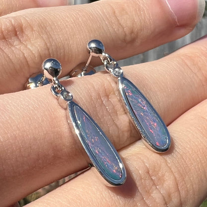 A pair of sterling silver, pear shaped opal doublet dangle earrings.  The opals have a gray body tone with red fire.