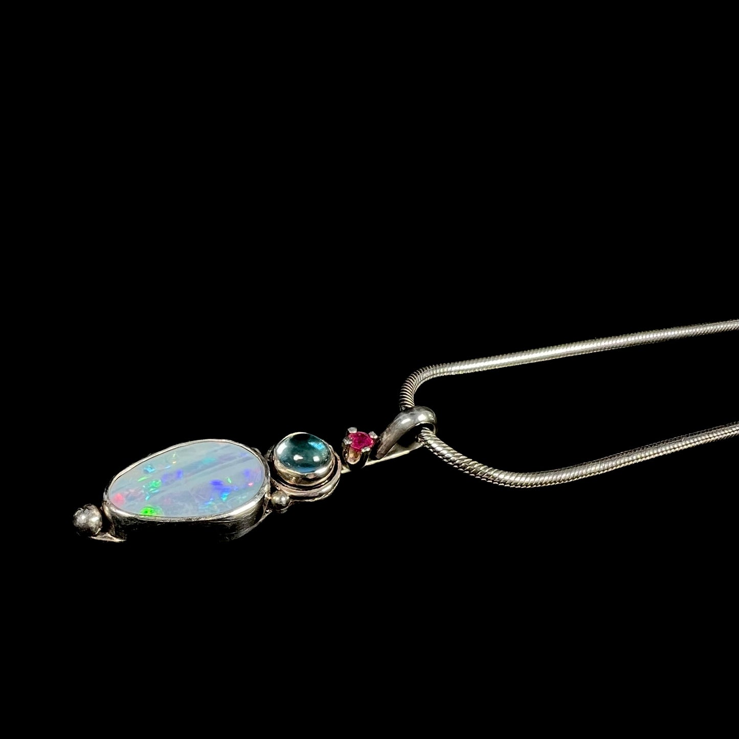 A sterling silver necklace shaped like a child, mounted with an opal doublet, a ruby, and a blue piece of glass.