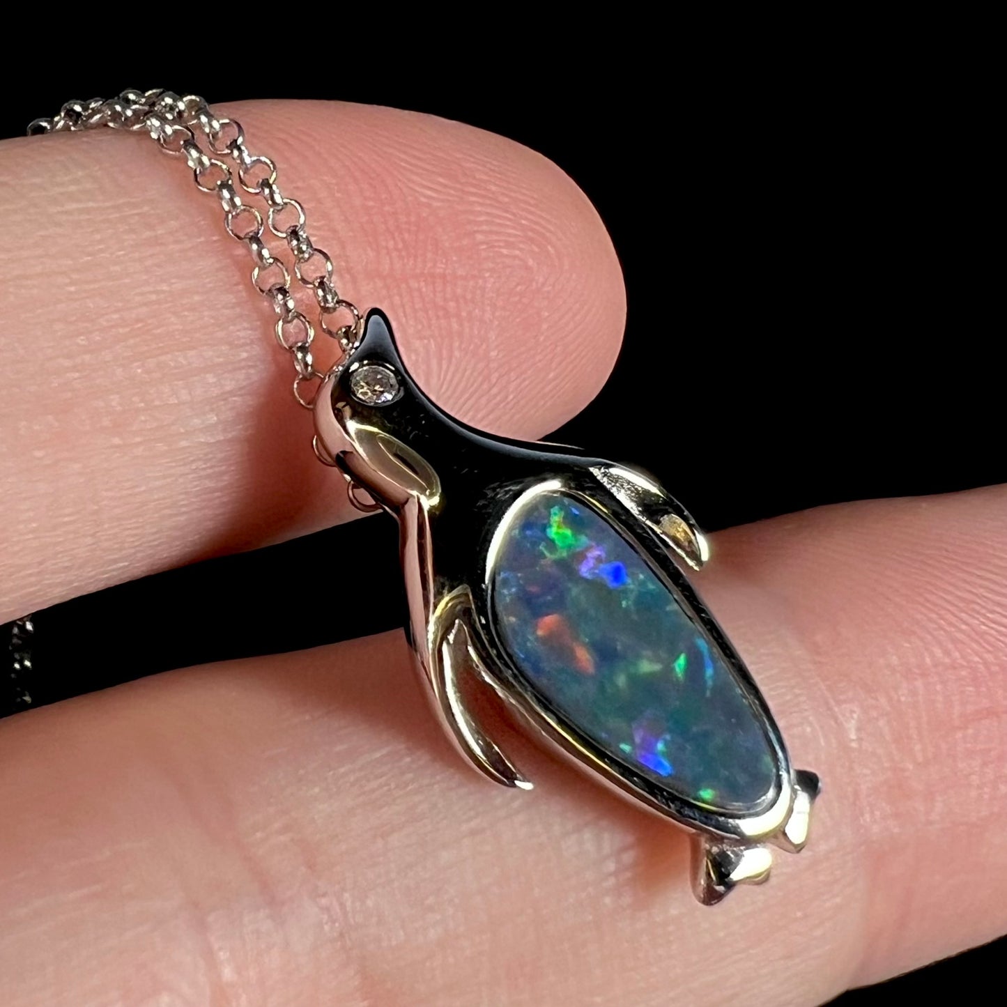 A sterling silver penguin necklace inlaid with a black opal doublet and a CZ accent in the penguin's eye.