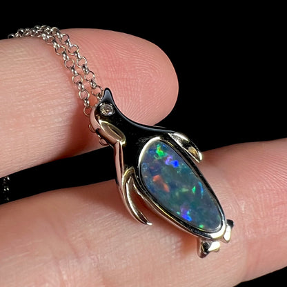 A sterling silver penguin necklace inlaid with a black opal doublet and a CZ accent in the penguin's eye.