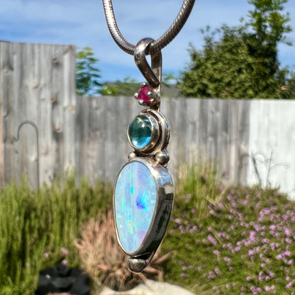 A sterling silver necklace shaped like a child, mounted with an opal doublet, a ruby, and a blue piece of glass.