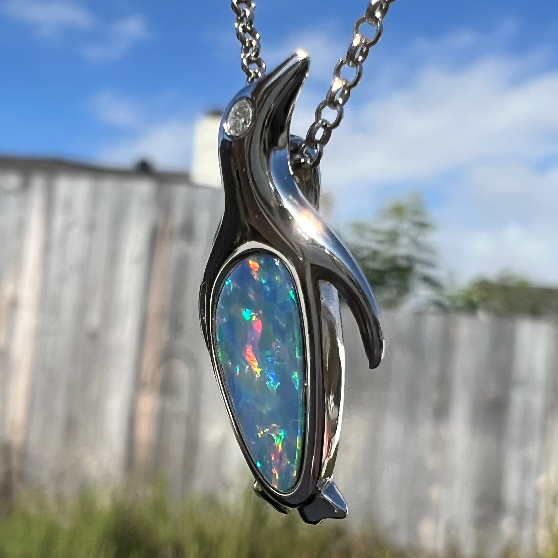 A sterling silver penguin necklace inlaid with a black opal doublet and a CZ accent in the penguin's eye.