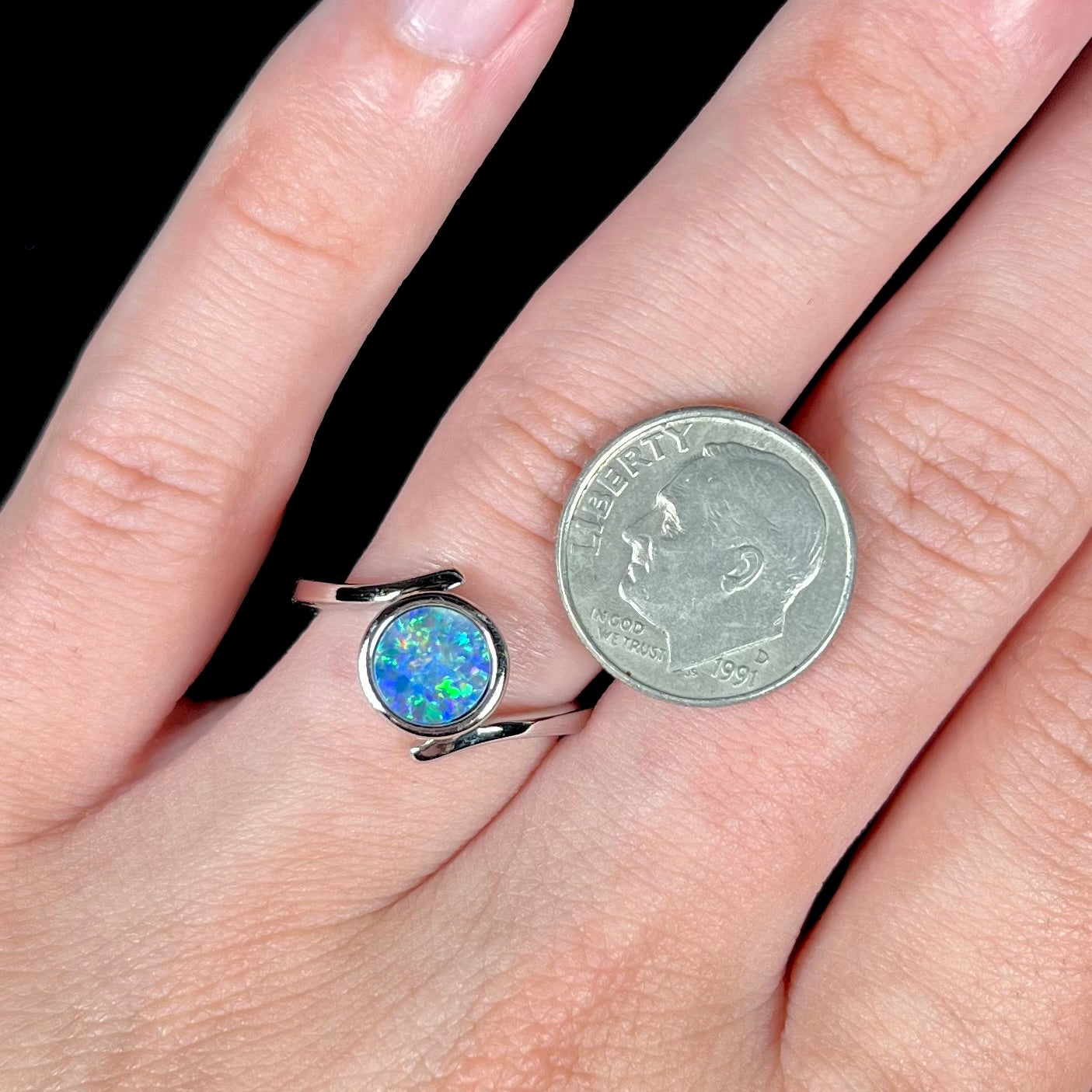 A sterling silver bypass ring bezel-set with a round cut black opal doublet.