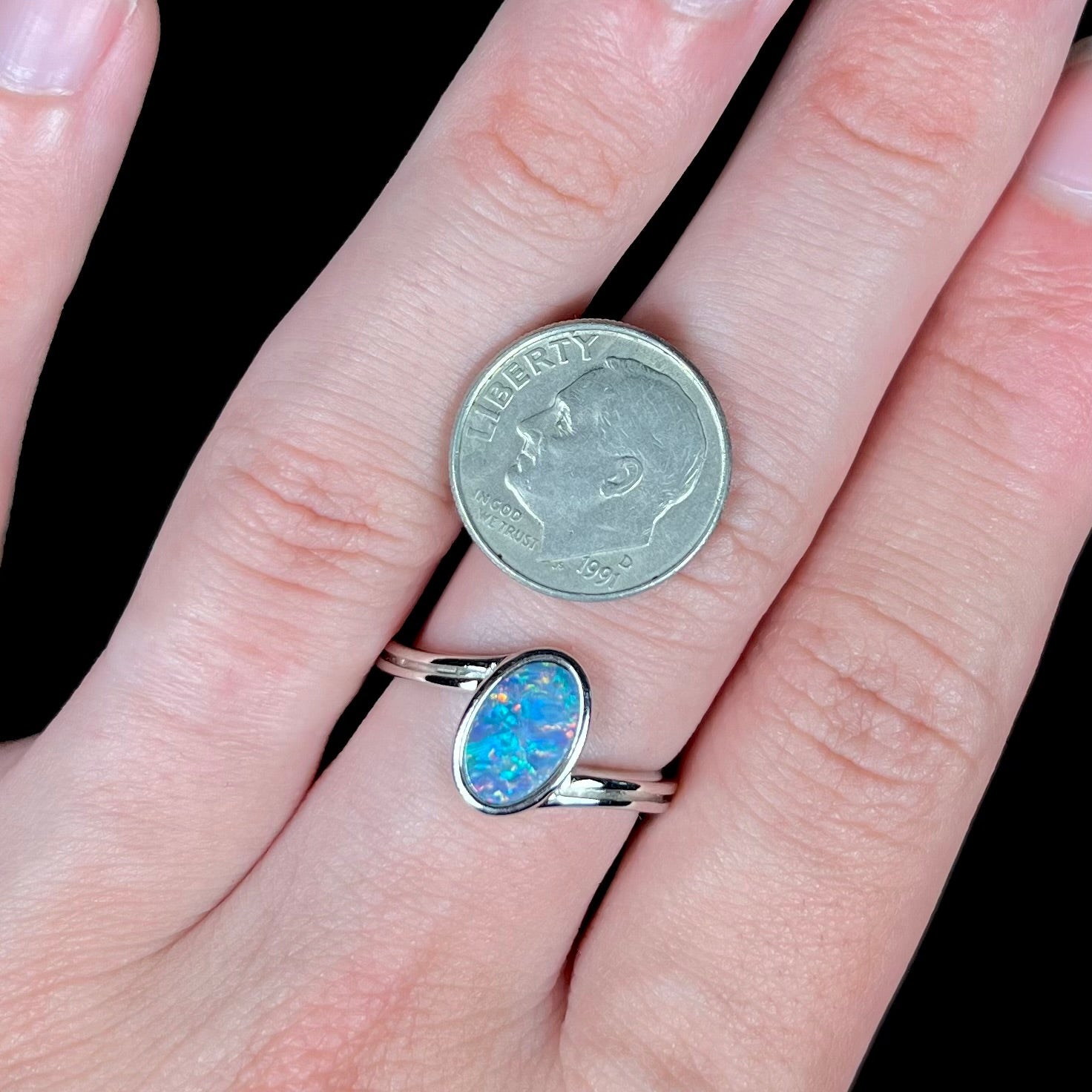 A sterling silver ring bezel-set with an oval shaped black opal doublet.  The opal has red and blue fire.