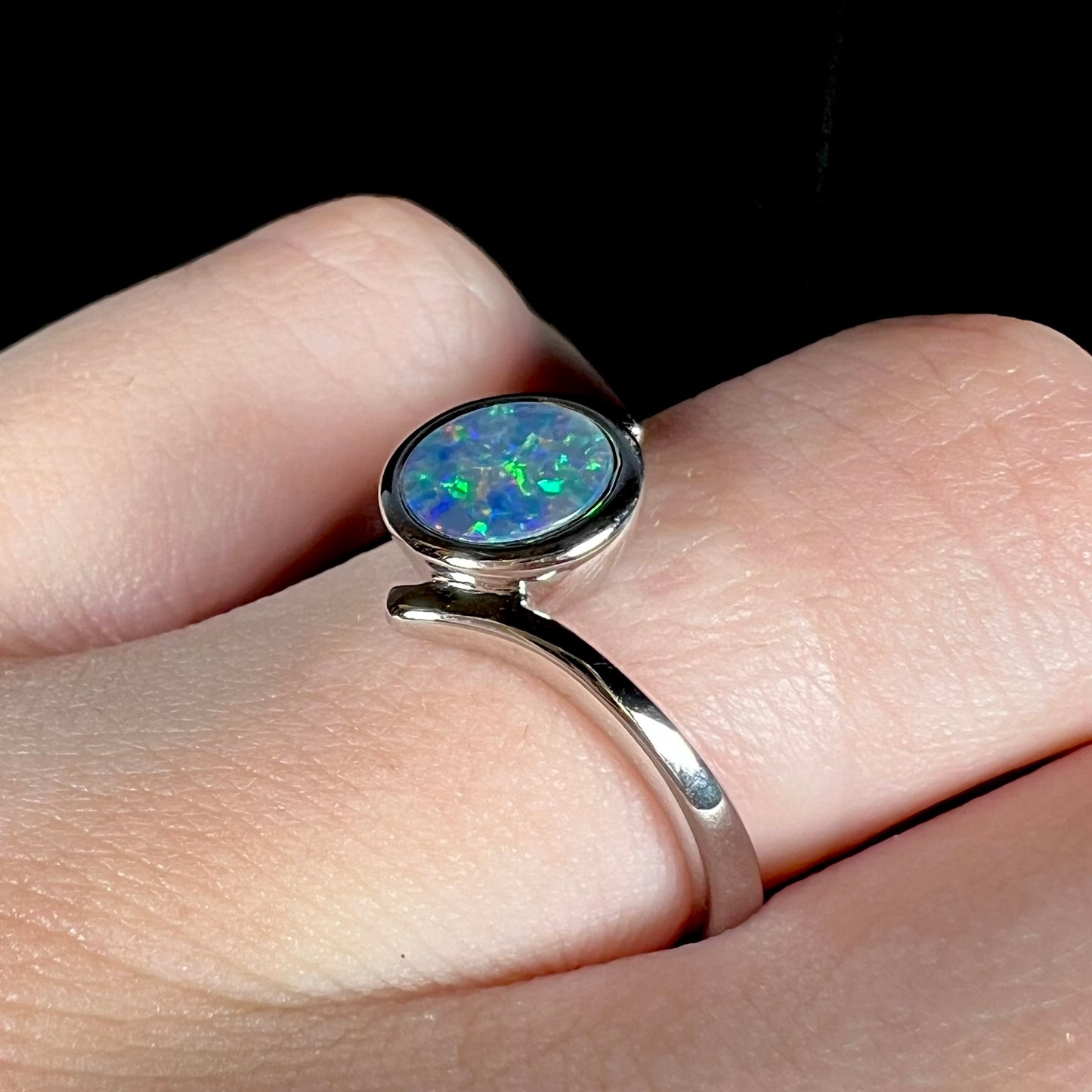 A sterling silver bypass ring bezel-set with a round cut black opal doublet.