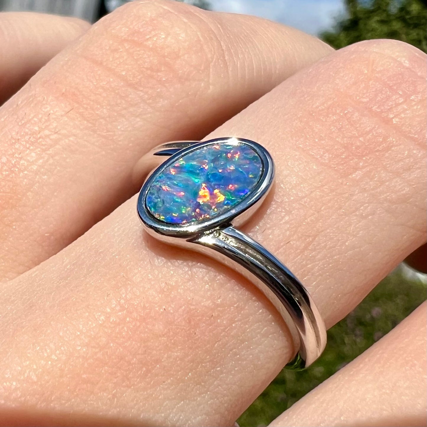 A sterling silver ring bezel-set with an oval shaped black opal doublet.  The opal has red and blue fire.