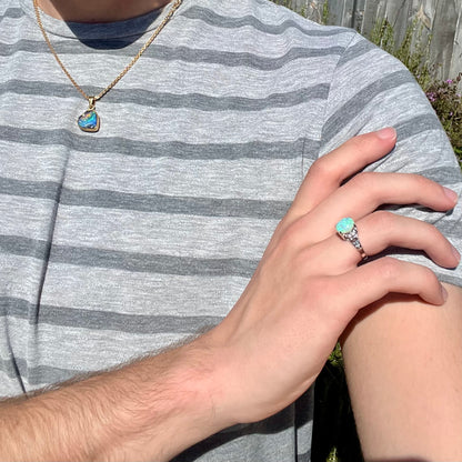 A platinum filigree ring mounted with a blue-green crystal opal and diamond accents.