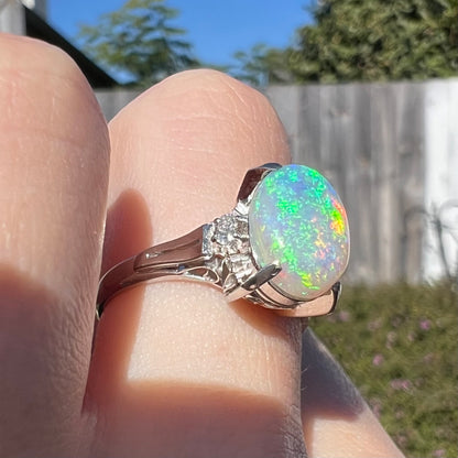 A platinum filigree opal engagement ring set with diamond accents.  The opal has green-blue colors.