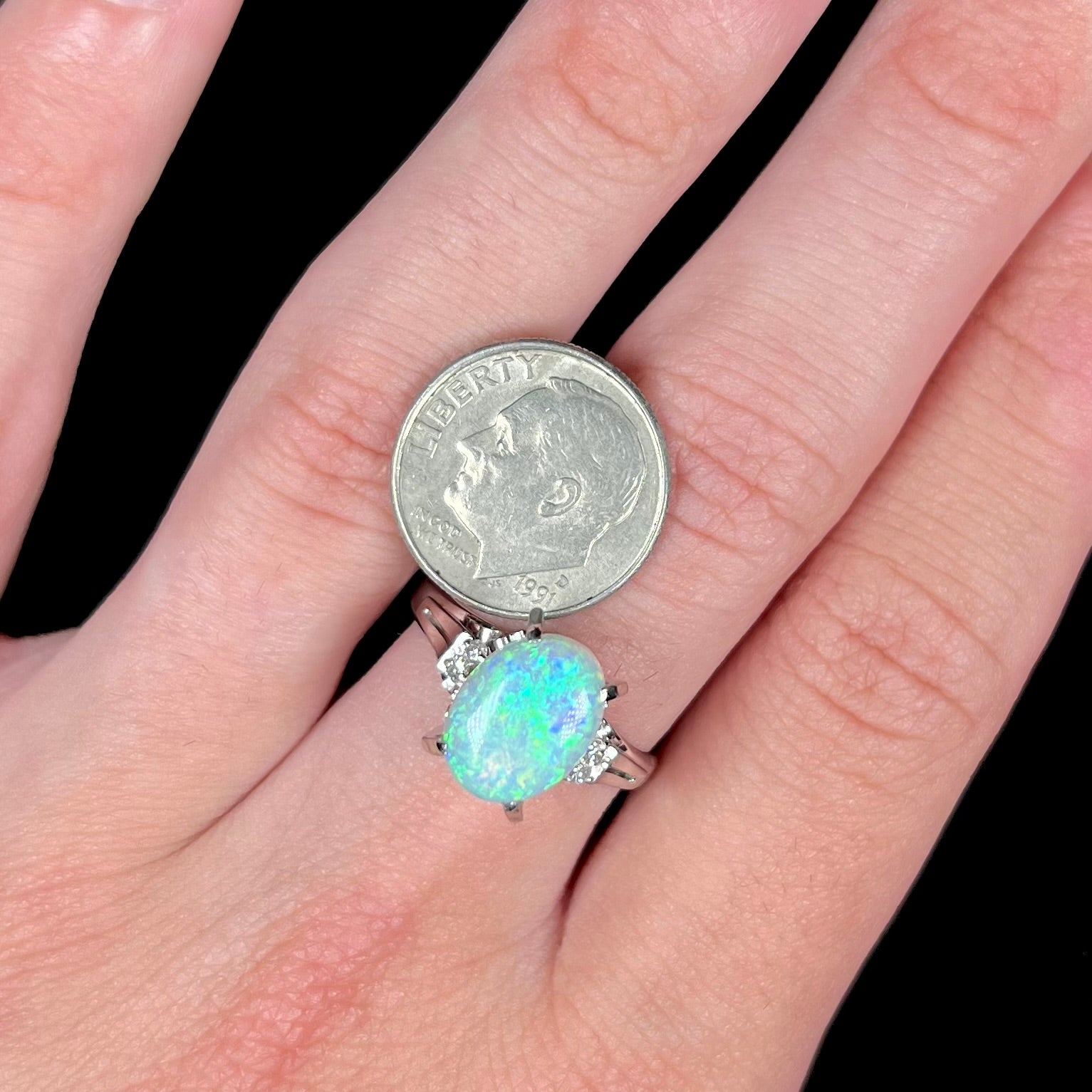 A platinum filigree opal engagement ring set with diamond accents.  The opal has green-blue colors.