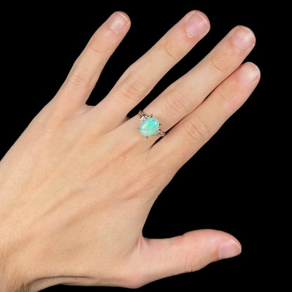 A platinum filigree opal engagement ring set with diamond accents.  The opal has green-blue colors.