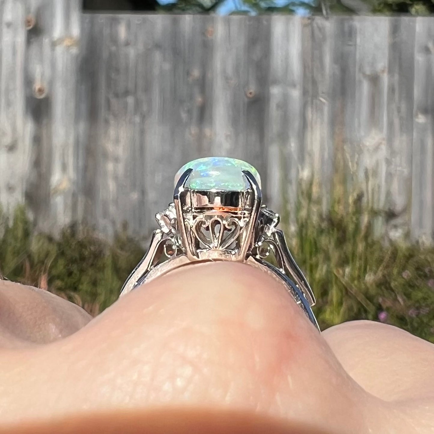 A platinum filigree opal engagement ring set with diamond accents.  The opal has green-blue colors.