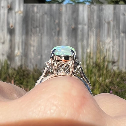 A platinum filigree opal engagement ring set with diamond accents.  The opal has green-blue colors.