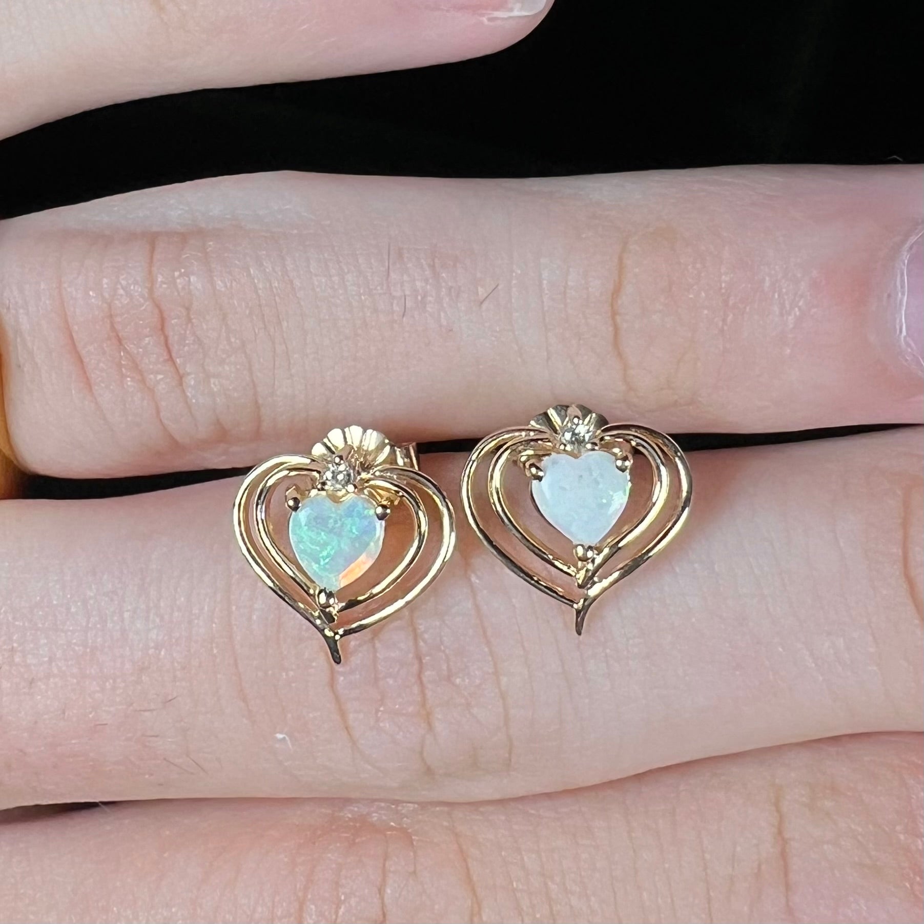 A pair of heart shaped, yellow gold opal stud earrings.  The top of the earrings have a diamond accent.