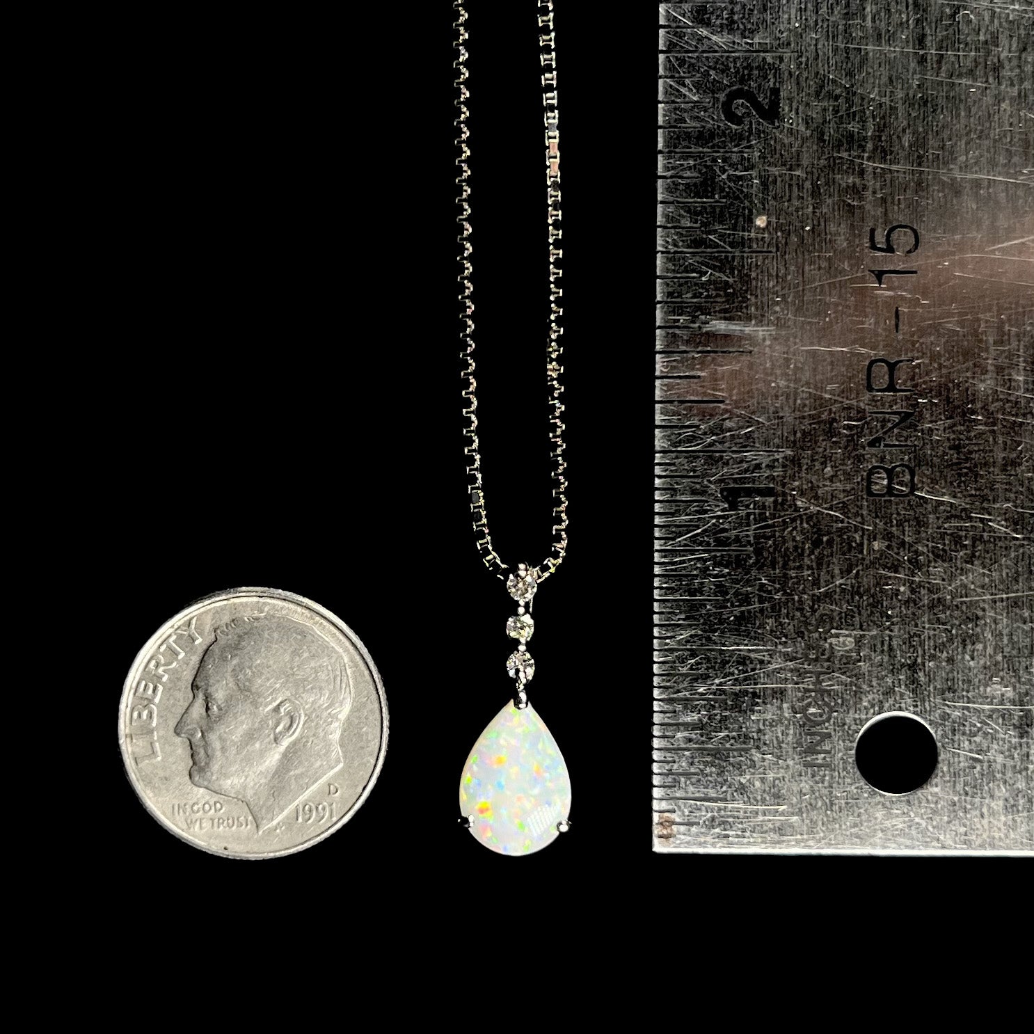 A platinum drop pendant mounted with three diamond accents and a pear shaped opal.