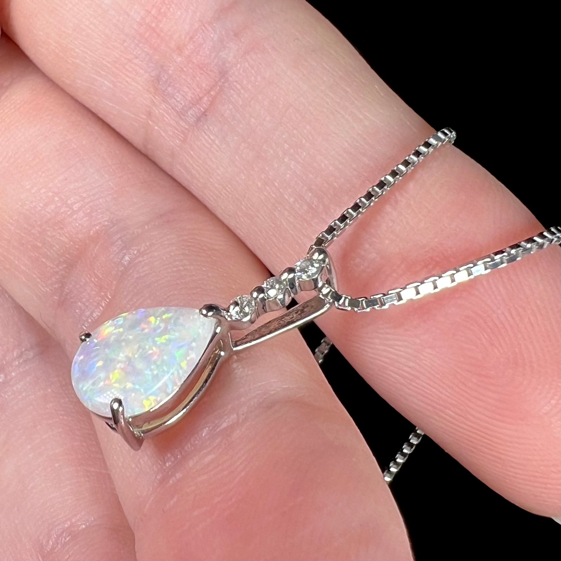 A platinum drop pendant mounted with three diamond accents and a pear shaped opal.