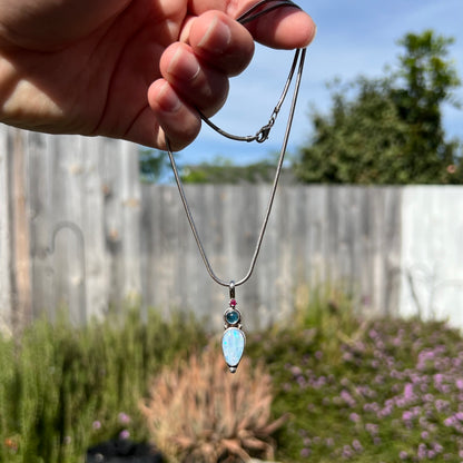 A sterling silver necklace shaped like a child, mounted with an opal doublet, a ruby, and a blue piece of glass.