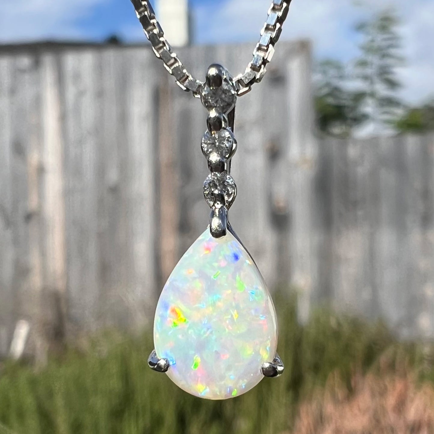 A platinum drop pendant mounted with three diamond accents and a pear shaped opal.