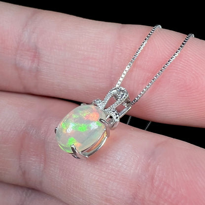 An oval cut Ethiopian opal mounted in a diamond-accented, 18 karat white gold pendant on a box chain.