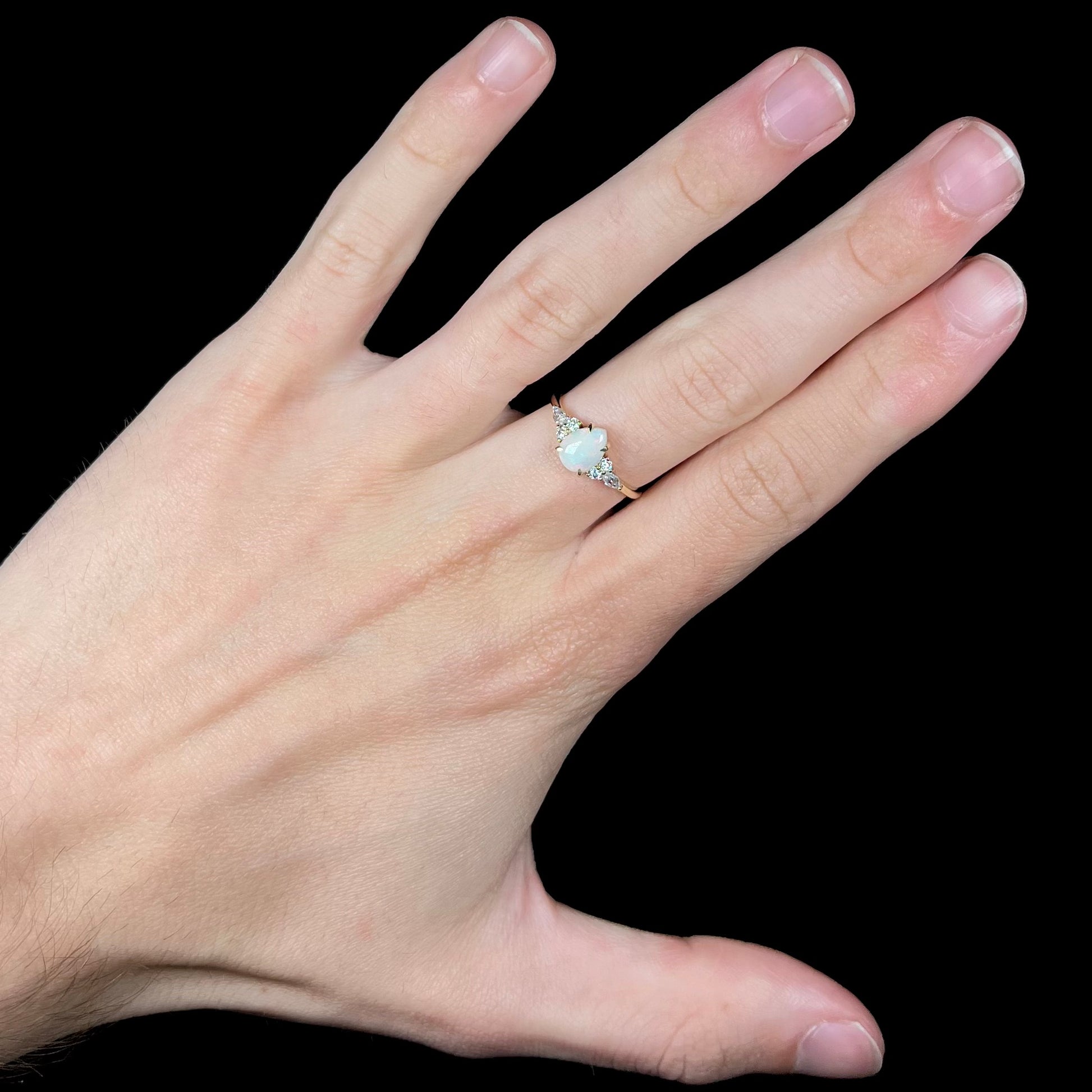 A dainty, pear shaped opal ring mounted in yellow gold with moissanite accents.