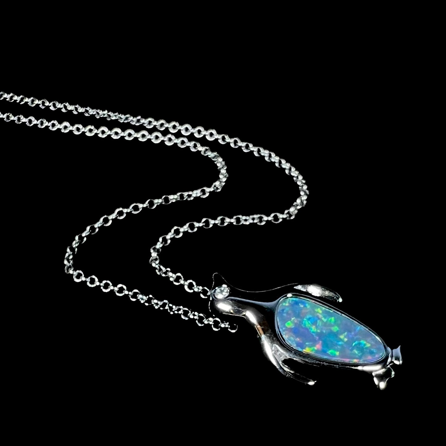 A sterling silver penguin necklace inlaid with a black opal doublet and a CZ accent in the penguin's eye.