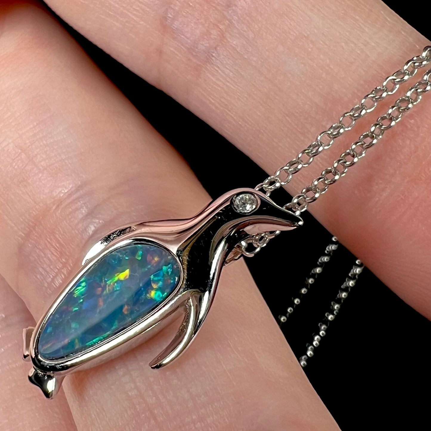 A sterling silver penguin necklace inlaid with a black opal doublet and a CZ accent in the penguin's eye.