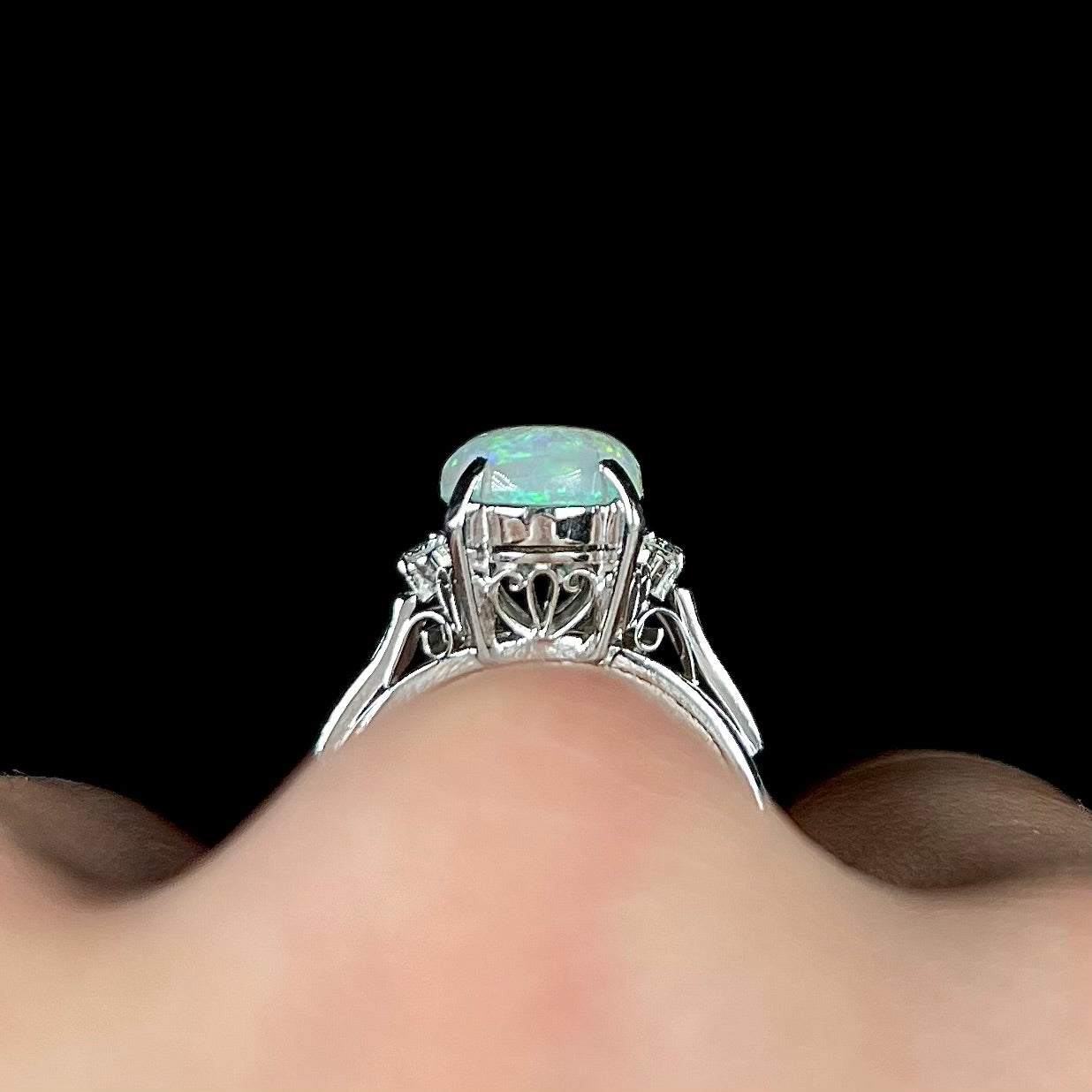 A platinum filigree opal engagement ring set with diamond accents.  The opal has green-blue colors.