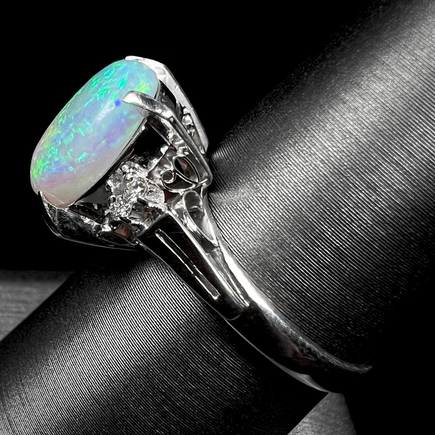 A platinum filigree opal engagement ring set with diamond accents.  The opal has green-blue colors.