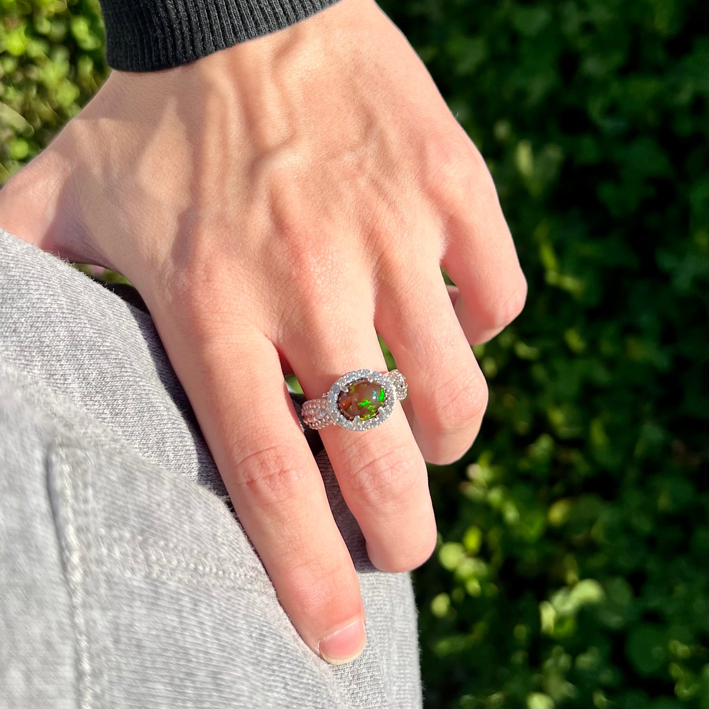 A CZ-accented sterling silver halo ring mounted with a smoked Ethiopian fire opal.  The opal plays green, red, and blue colors.