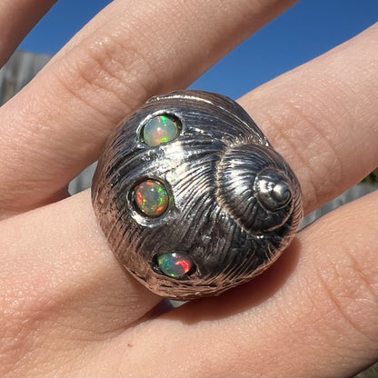 A large, three dimensional sterling silver snail seashell ring set with three round Ethiopian fire opal stones.