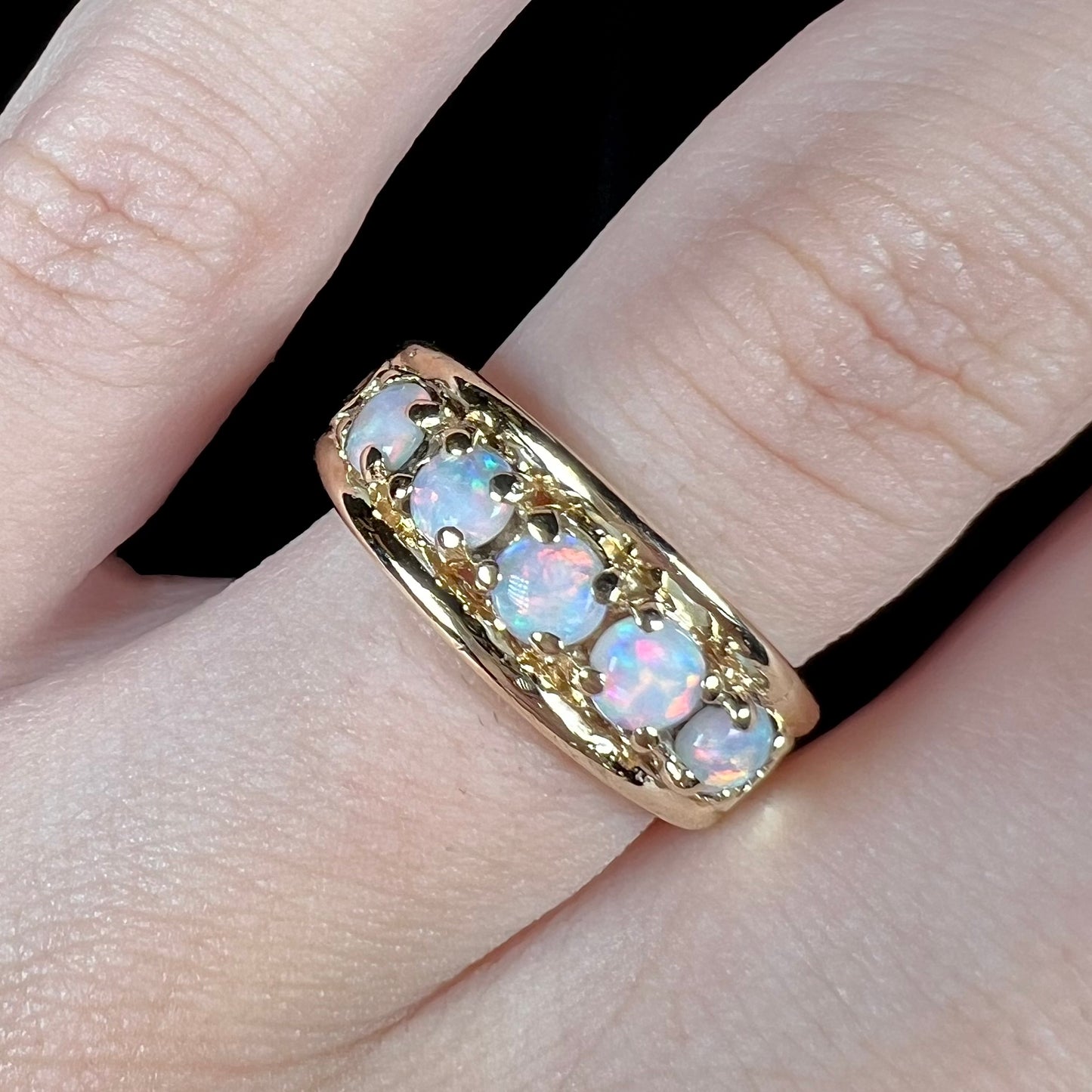 A yellow gold band set with five round cabochon cut opals and heart design accents.