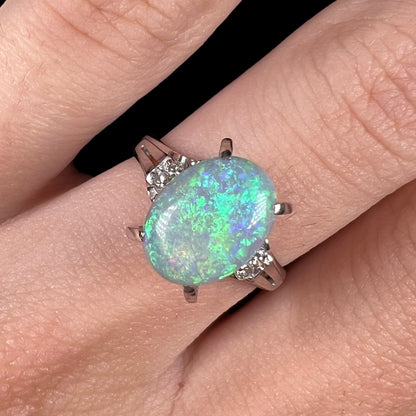 A platinum filigree opal engagement ring set with diamond accents.  The opal has green-blue colors.