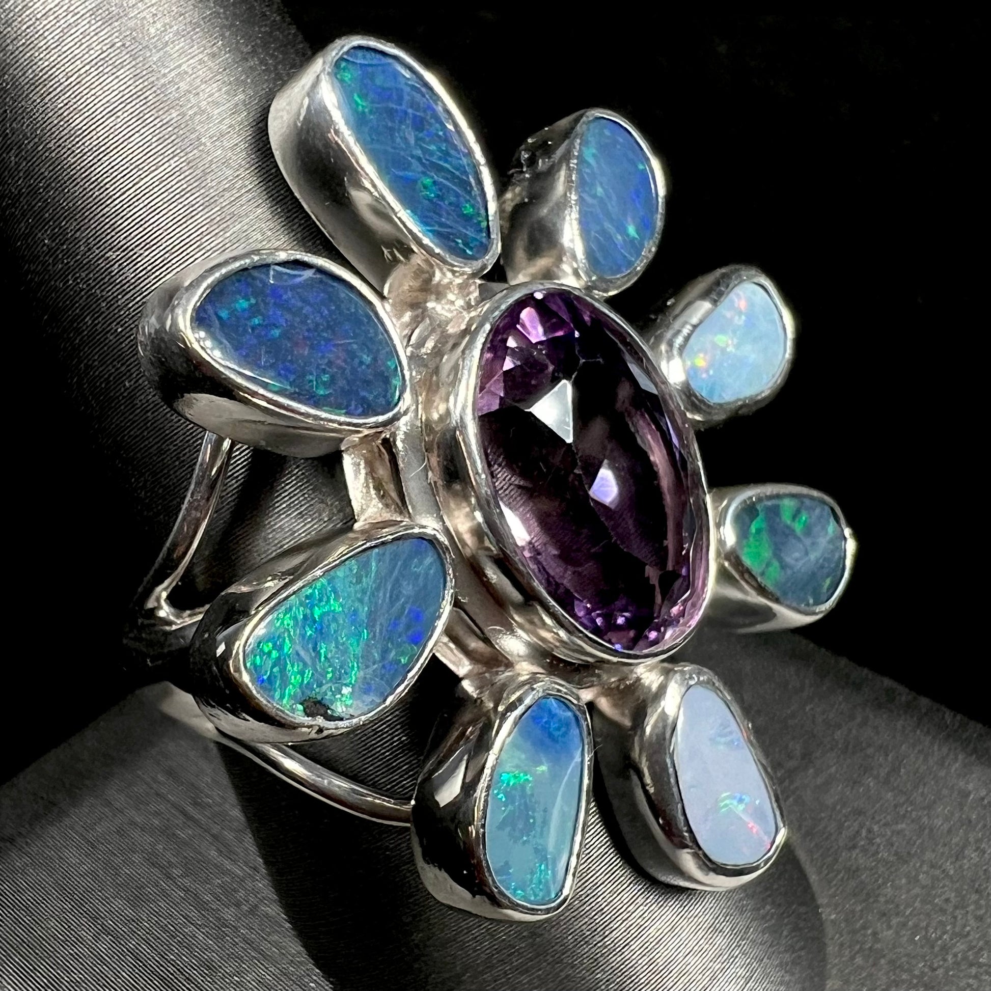 A sterling silver flower shaped ring set with an oval cut amethyst in the center and black opal doublet petals.