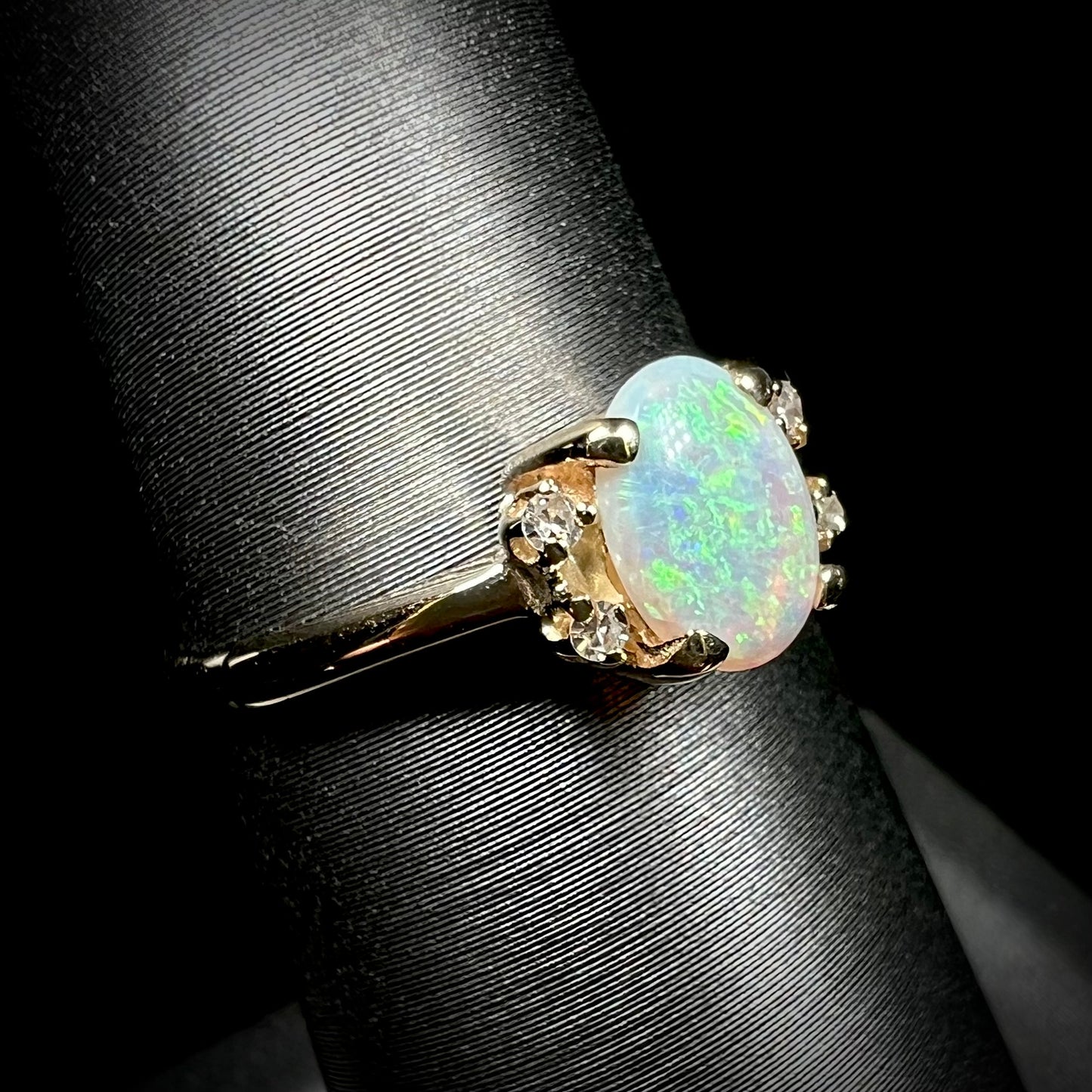 A dainty yellow gold ring set with a Coober Pedy opal with green flashfire pattern and diamond accents.