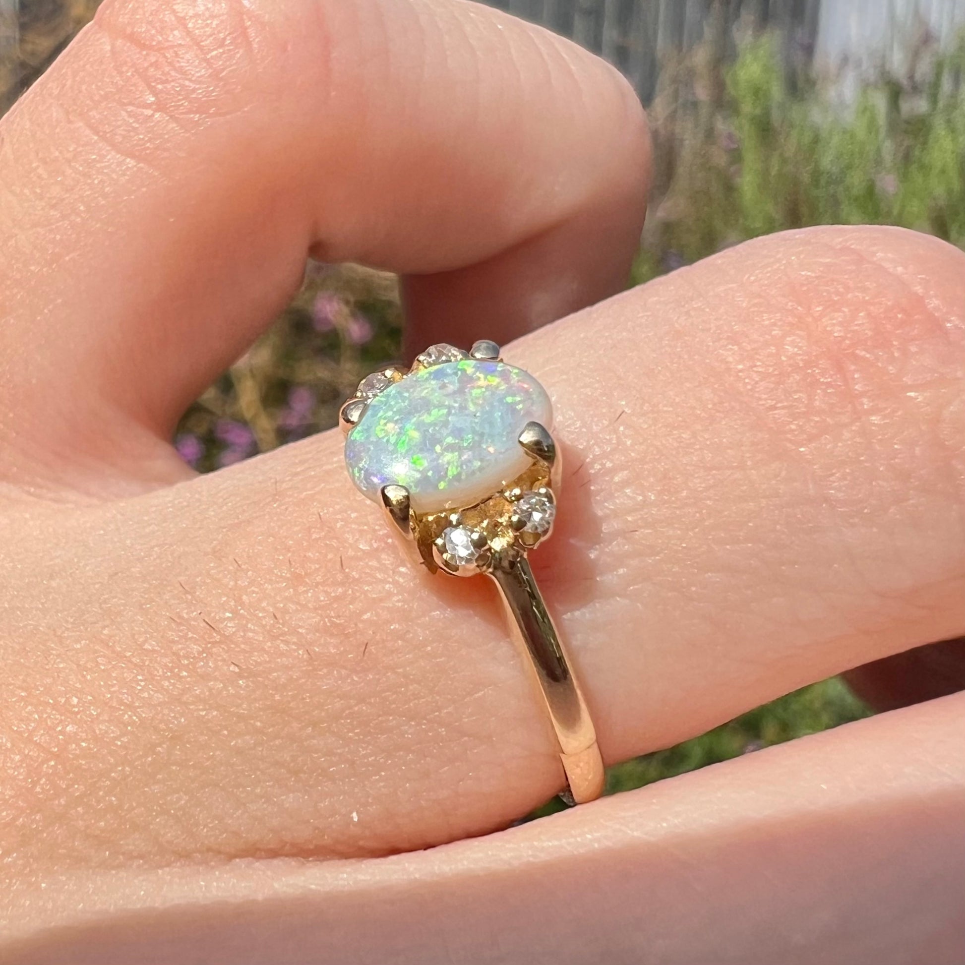 A dainty yellow gold ring set with a Coober Pedy opal with green flashfire pattern and diamond accents.