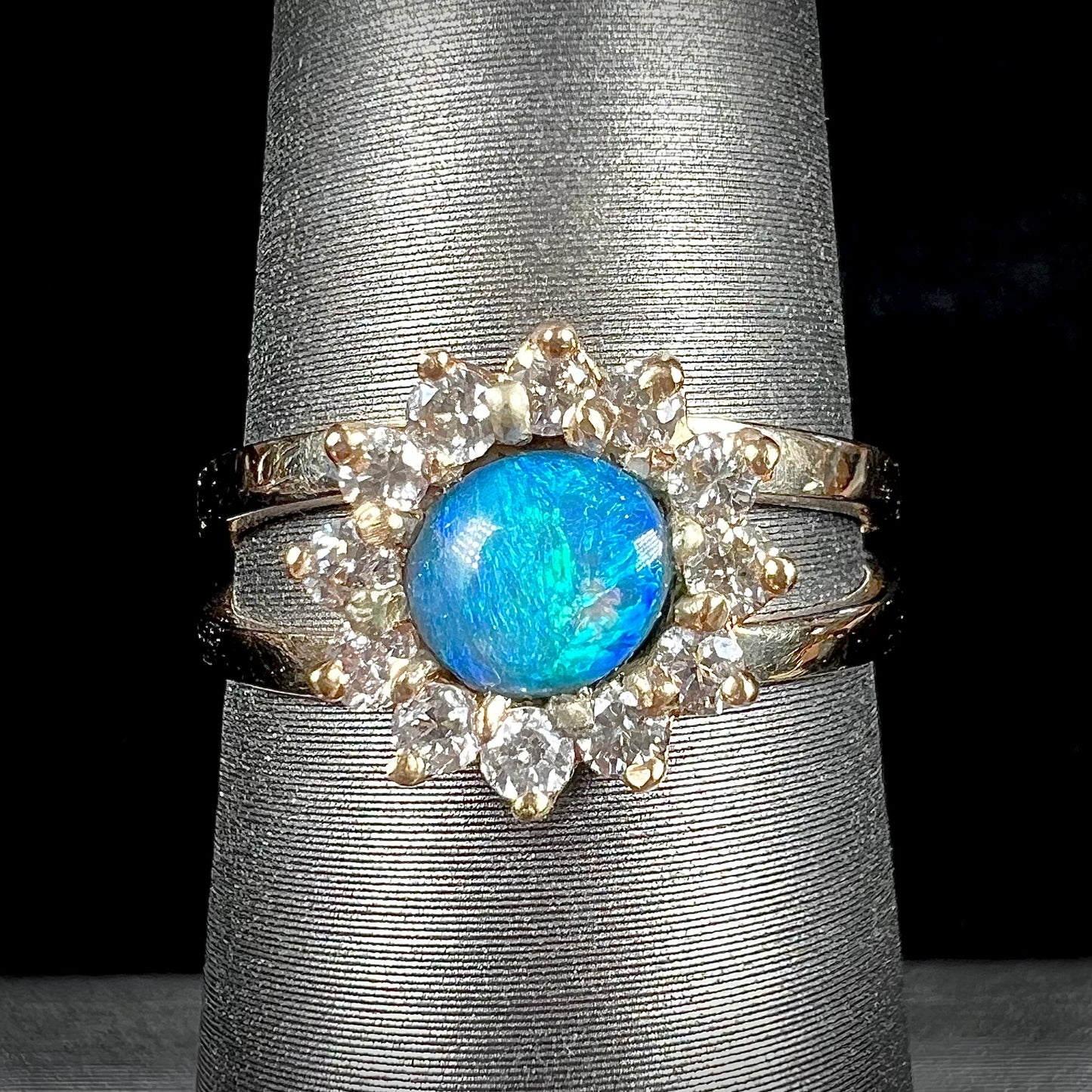 A ladies' round cut black opal and diamond halo ring.  The ring is yellow gold and has a split shank.