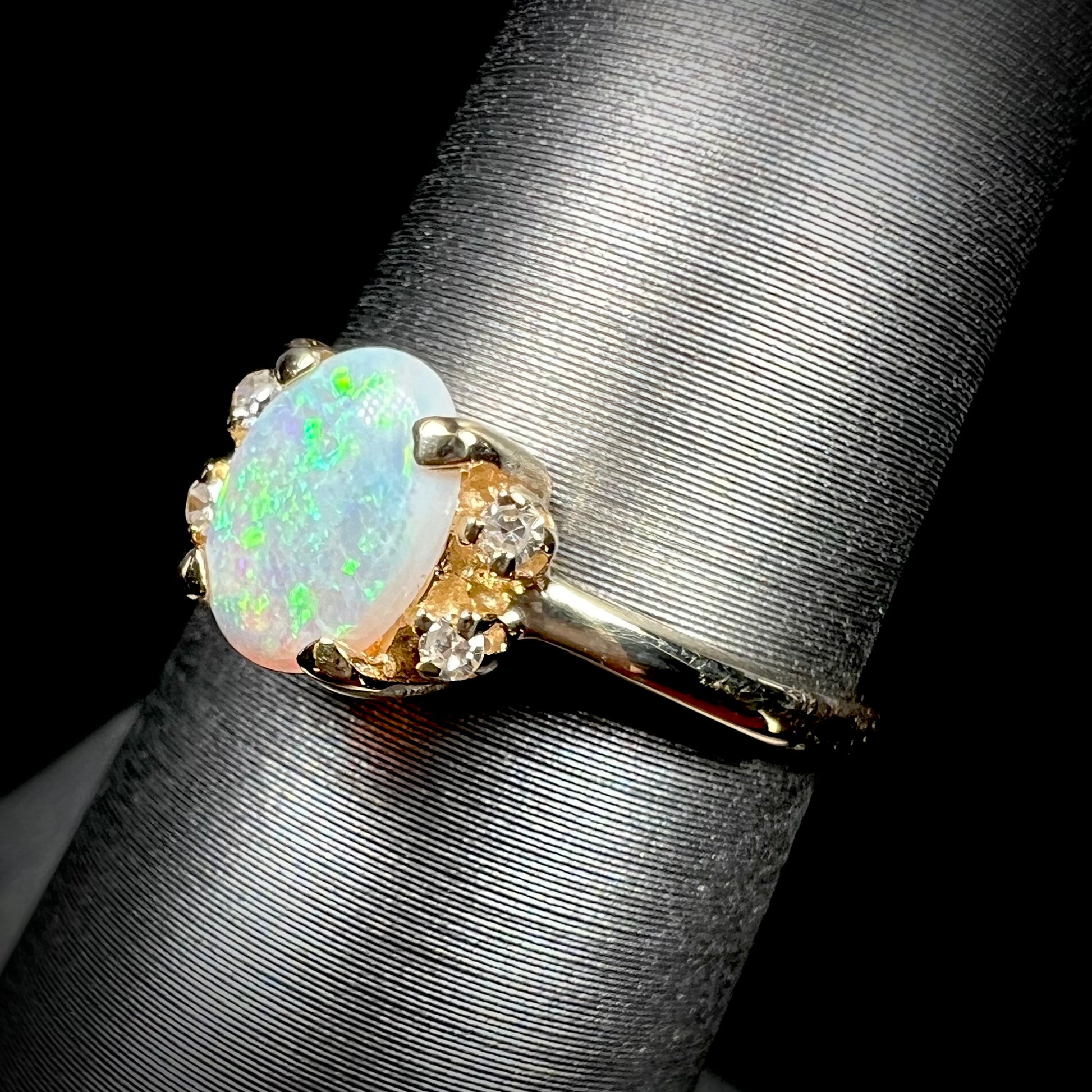 A dainty yellow gold ring set with a Coober Pedy opal with green flashfire pattern and diamond accents.