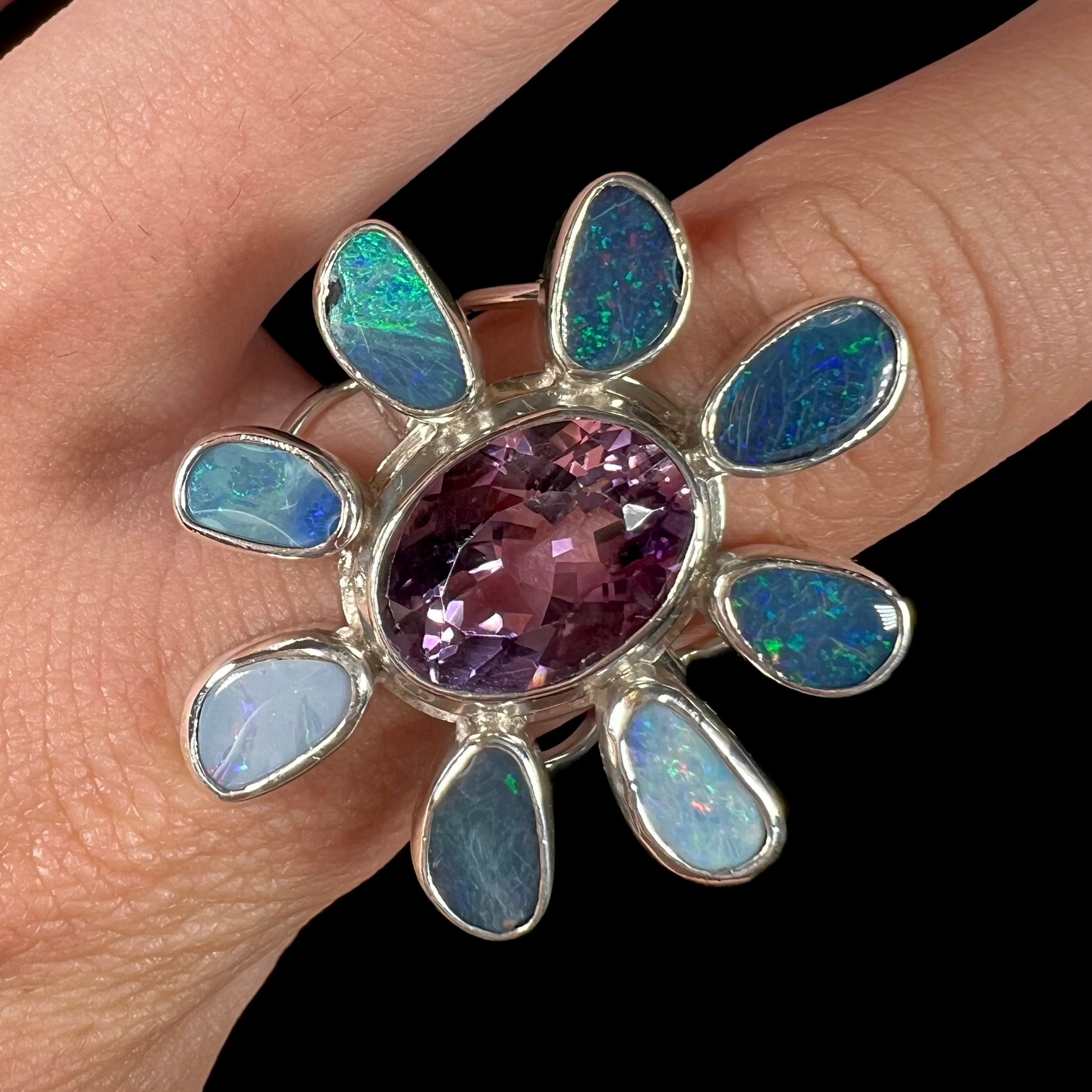 A sterling silver flower shaped ring set with an oval cut amethyst in the center and black opal doublet petals.