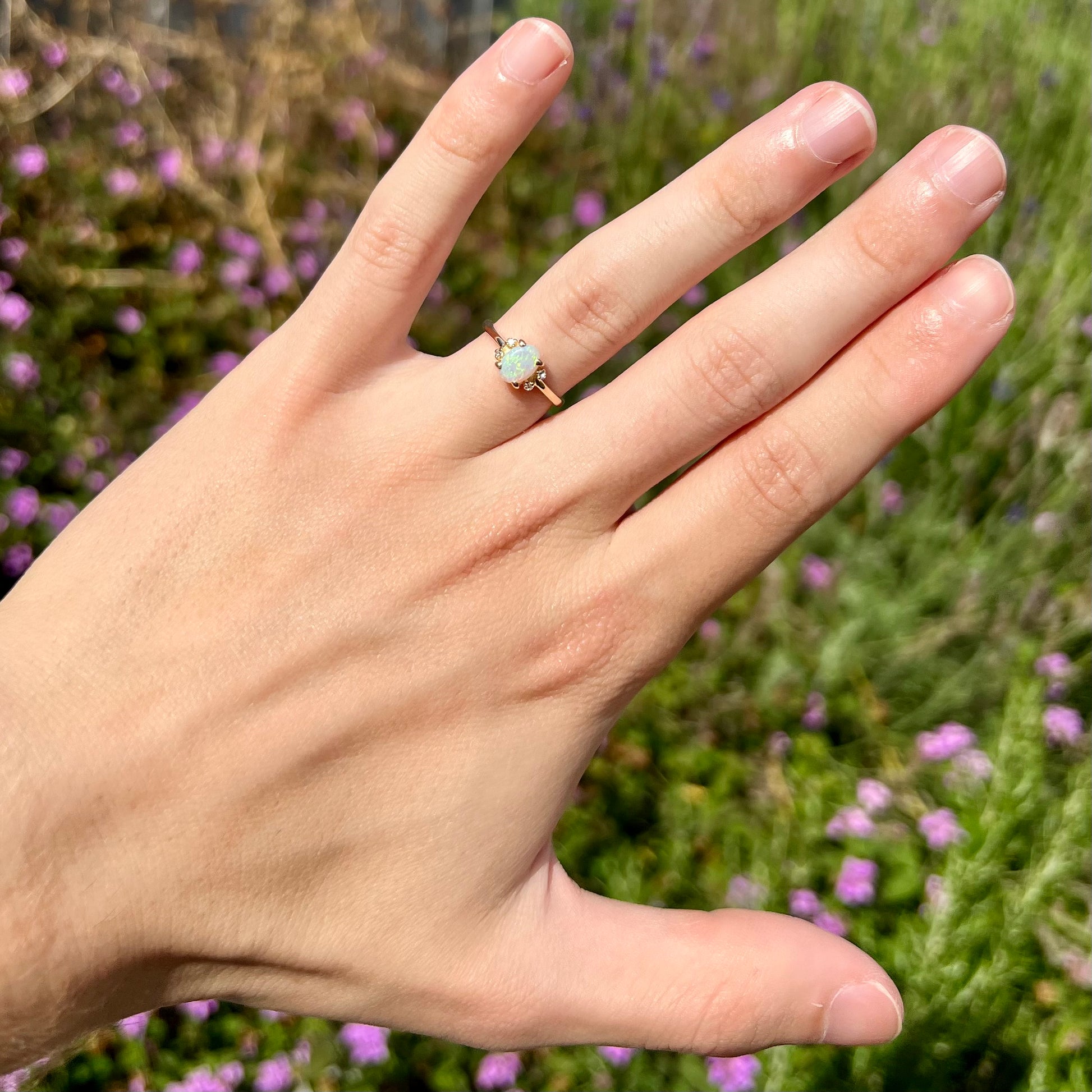 A dainty yellow gold ring set with a Coober Pedy opal with green flashfire pattern and diamond accents.