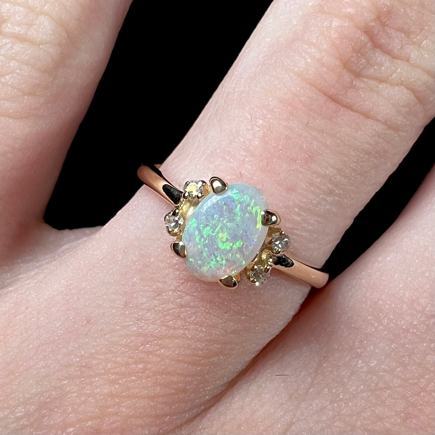 A dainty yellow gold ring set with a Coober Pedy opal with green flashfire pattern and diamond accents.