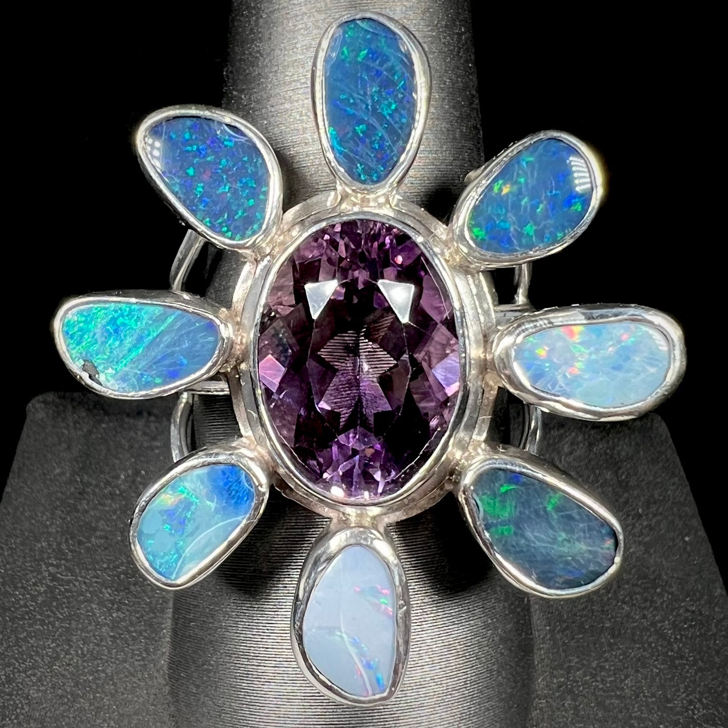 A sterling silver flower shaped ring set with an oval cut amethyst in the center and black opal doublet petals.