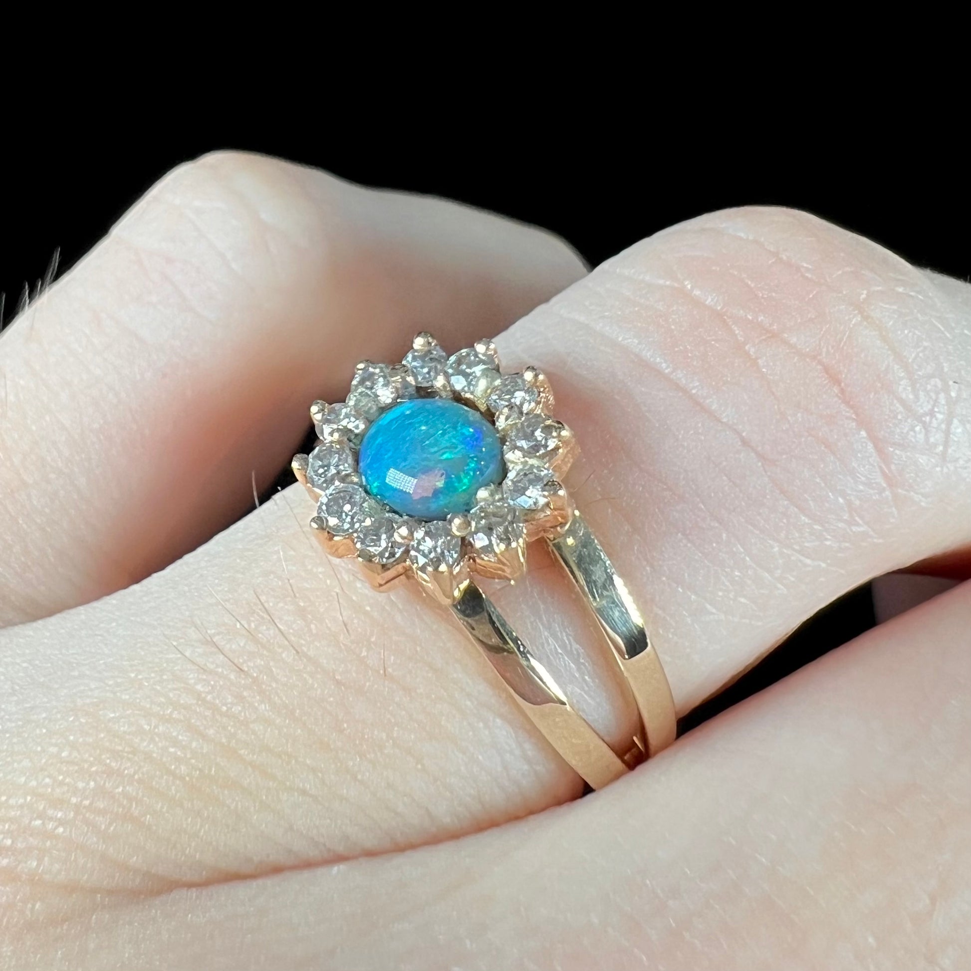 A ladies' round cut black opal and diamond halo ring.  The ring is yellow gold and has a split shank.