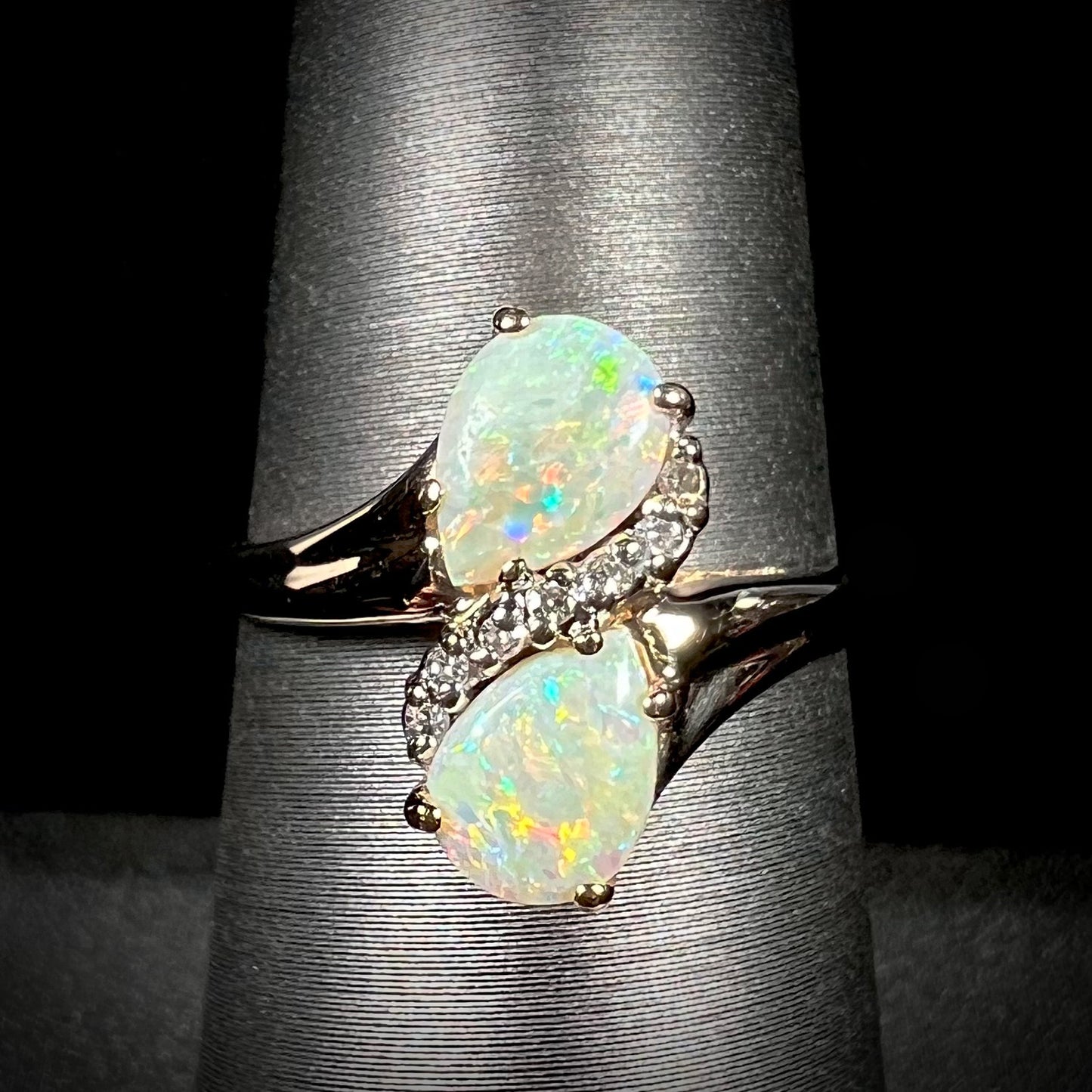 A yellow gold ring mounted with two pear shaped opals and diamond accents  The stones form an infinity shaped design.