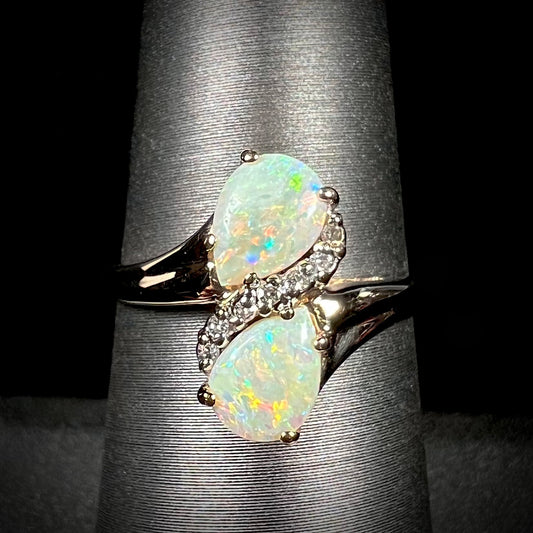 A yellow gold ring mounted with two pear shaped opals and diamond accents  The stones form an infinity shaped design.