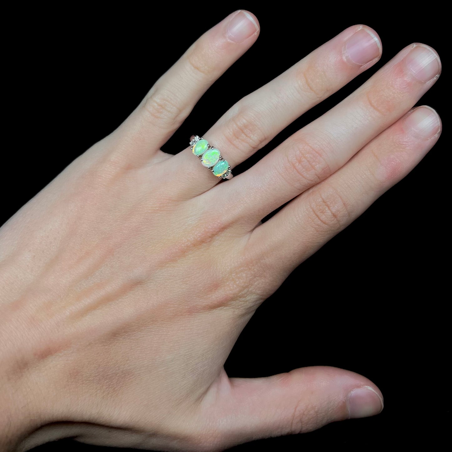 A ladies' white gold ring prong-set with three natural white opals and diamond accents.  The opals play a green color.