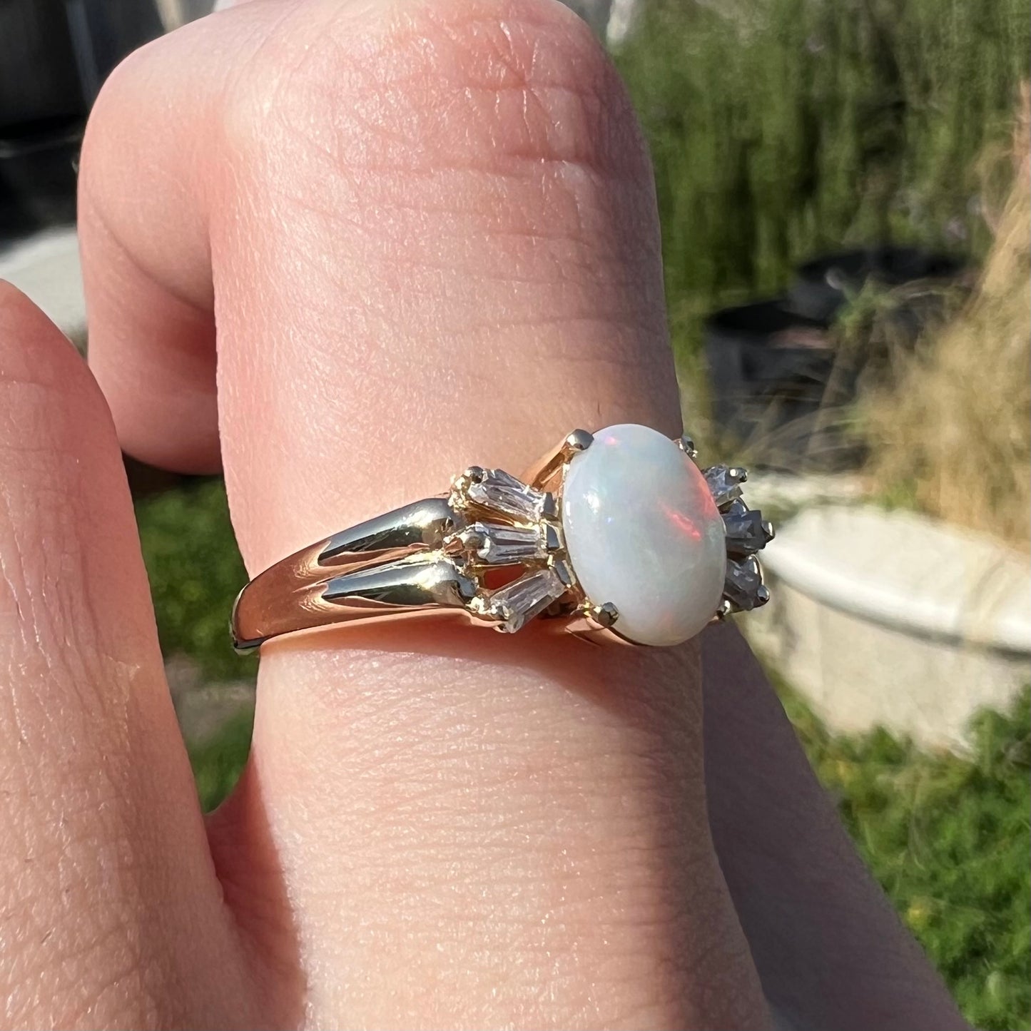 A yellow gold ring set with a natural Australian opal and tapered baguette cut cubic zirconia accents.