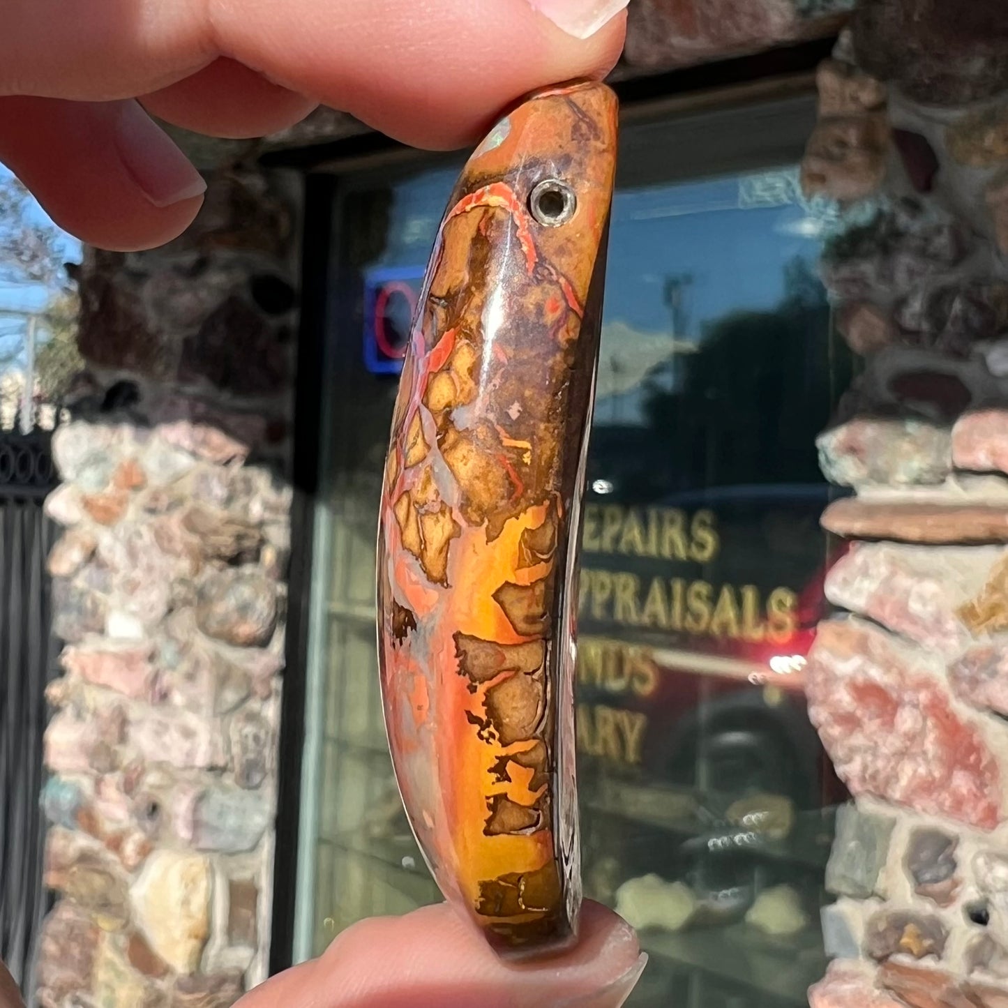 A polished boulder opal stone from Koroit, Australia.  The stone has been drilled with a bead hole.