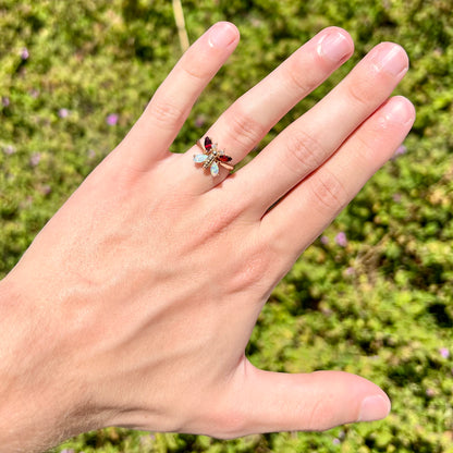 A yellow gold butterfly ring mounted with marquise cut garnets and opals and round diamond accents.